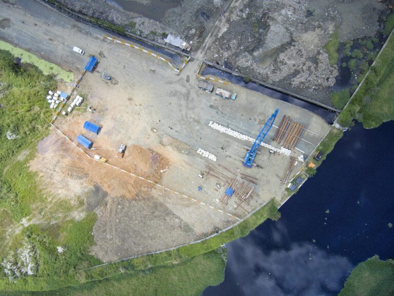High-angle shot of construction site by a river in the Philippines, featuring cranes and machinery.